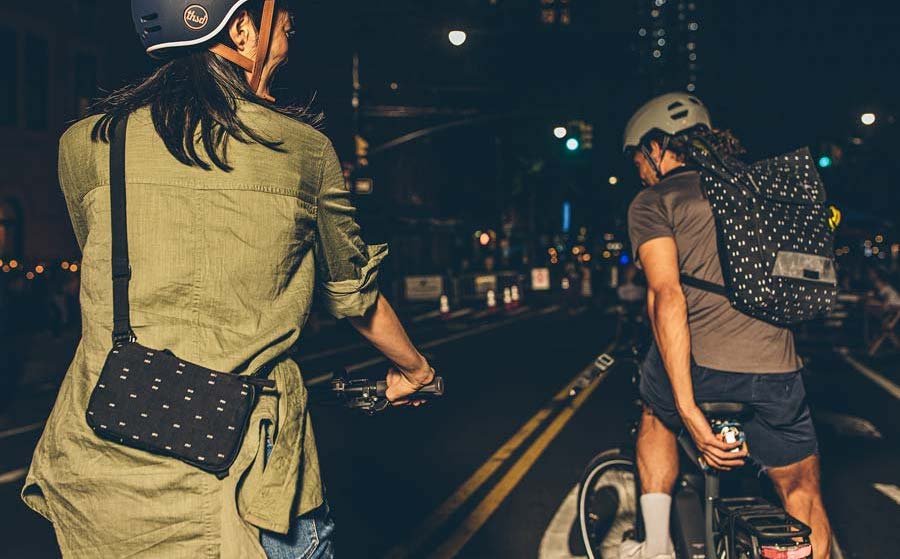 Two people on bikes wearing reflective bike bags at night.